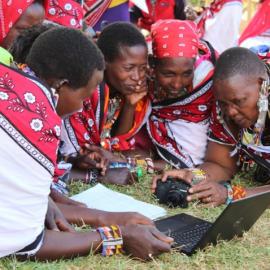 Local women crouch over a computer learning camera skills.